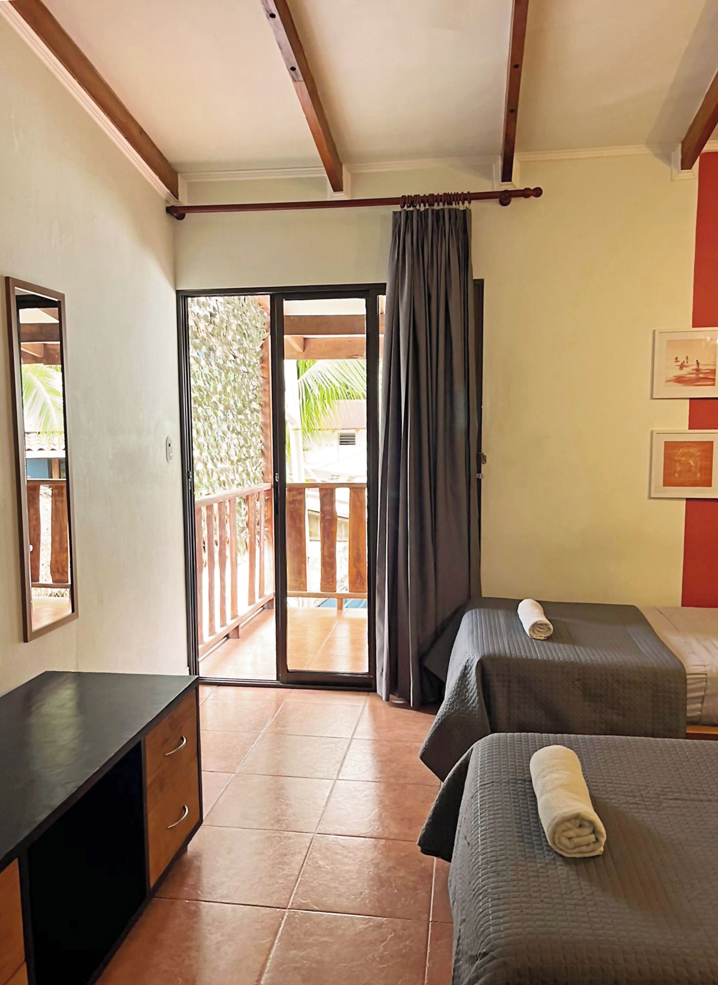 A hotel room with a balcony, two beds, a desk, and a sliding door to the outside.