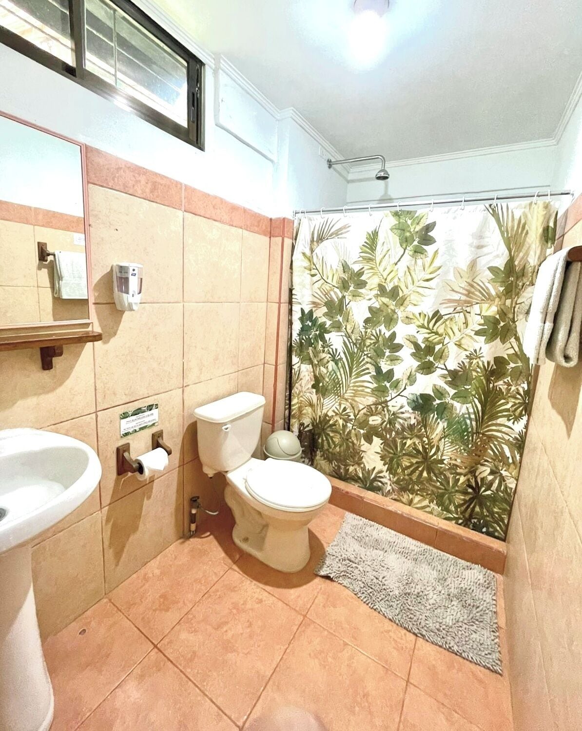 A bathroom with a toilet, sink, and shower curtain with a leaf pattern.