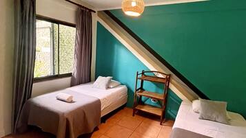 A room with two single beds, a wooden chair, a window with curtains, and a ceiling fan.