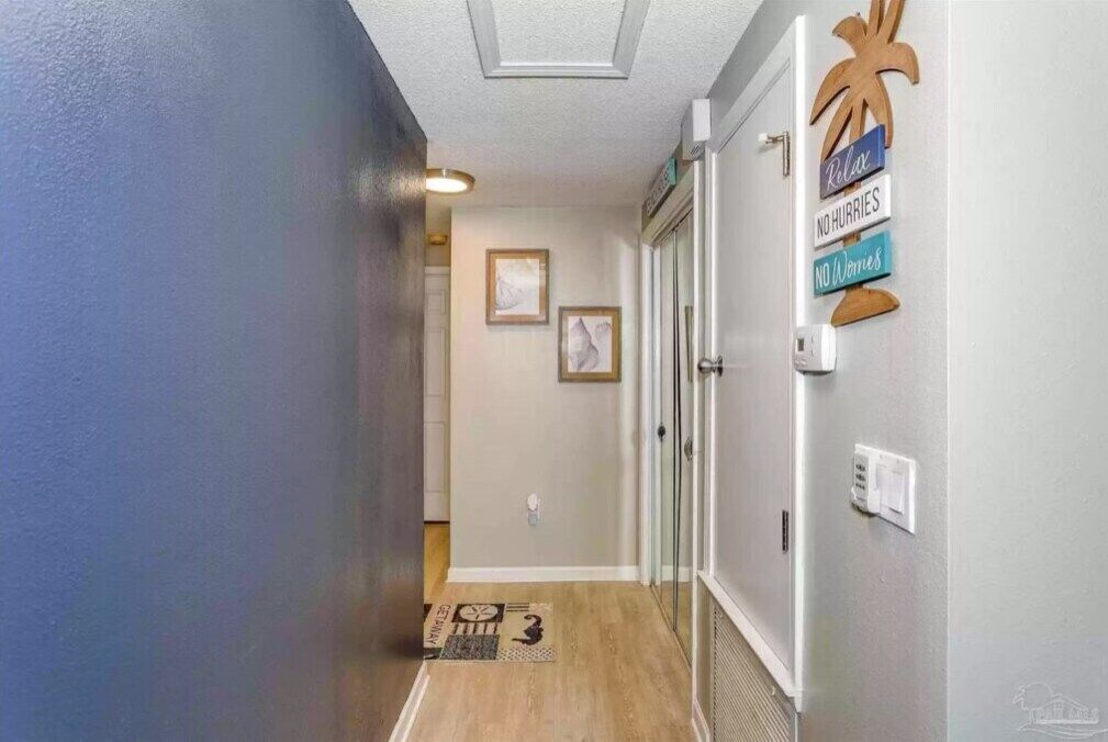 A hallway with a wooden floor, a doormat, and a wall with a palm tree and signs saying "Relax," "No Hurries," and "No Worries."
