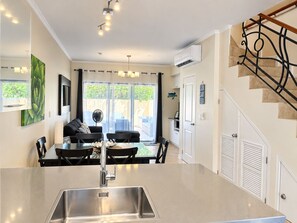 A modern kitchen with a central island, a dining area with a black table and chairs, and a staircase with a decorative railing.