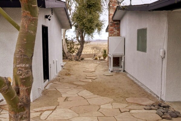 Un étroit sentier mène à un bâtiment à l’extérieur blanc, dont une partie est en briques.