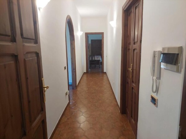 Un pasillo con puertas de madera, suelo de baldosas y un teléfono en la pared.