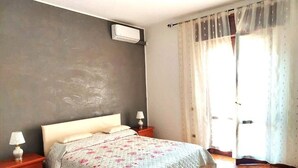 A bedroom with a bed, two bedside tables, a wall-mounted air conditioner, and a window with curtains. - IN THE COUNTRYSIDE BETWEEN THE SEA AND THE MOUNTAINS (Lazio)