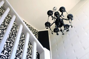 Una escalera blanca con barandales de diseño negro y un candelabro negro con motivos florales.