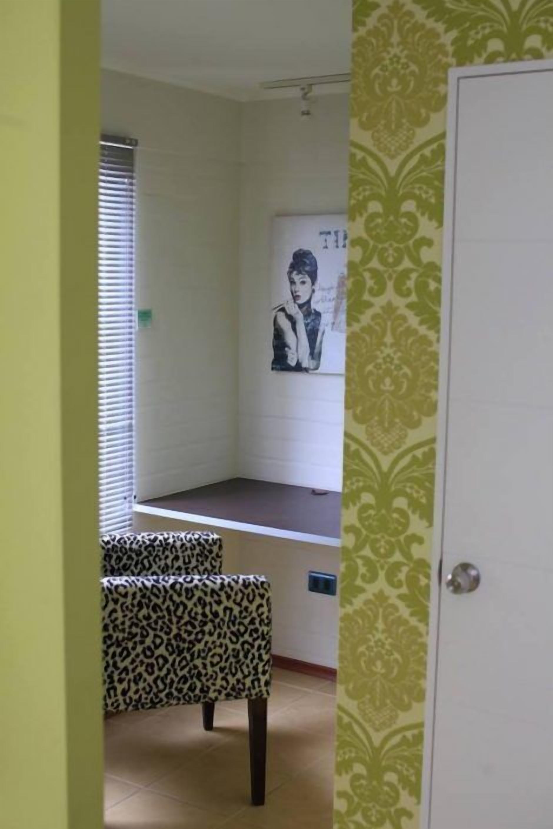 A room with a white desk, a leopard print bench, a poster on the wall, and a patterned wallpaper on one side.
