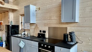 Une cuisine moderne avec des murs recouverts de panneaux en bois, des meubles gris, un plan de travail noir et des appareils en acier inoxydable, notamment une cuisinière, un four et une machine à café.