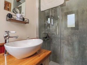 A bathroom with a white vessel sink, a wooden countertop, a glass shower enclosure, and a mirror with a towel rack above it.
