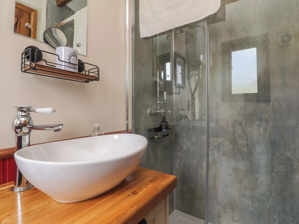 Un bagno con un lavabo a incasso bianco, un piano in legno, un box doccia in vetro e uno specchio con porta asciugamani sopra.