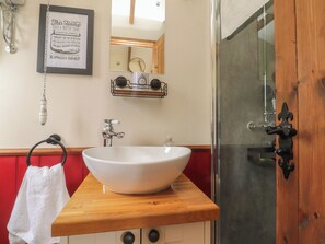 Un bagno con un lavandino bianco, uno specchio, un portascopevoli e un cartello incorniciato.