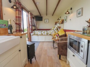 Une cuisine chaleureuse avec un four encastré, un coin repas avec une banquette et une fenêtre avec des rideaux.
