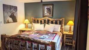 A bed with a rustic wooden headboard, two bedside lamps, and a quilt with animal prints. - Cute and Economical Studio with King Bed (Estes Park)
