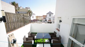 A balcony with a table and chairs, a wooden fence, and a view of buildings in the background. - 55 Livingtarifa Los 4 vientos (Tarifa)
