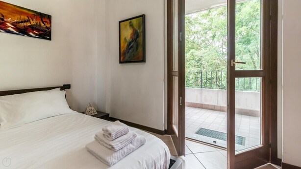 Un dormitorio con cama, un cuadro y un balcón con vistas a árboles.