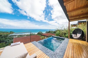 A rooftop infinity pool with a wooden deck, a hanging chair, and a view of the ocean.