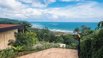 Um terraço com vista para o oceano e vegetação ao redor.