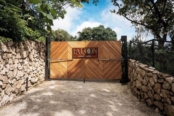 A gated entrance to LALON Luxury Suites with a stone wall and wooden gate.