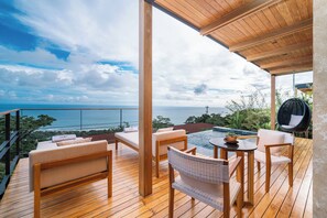 A wooden deck with outdoor seating, a small table, and a view of the ocean.