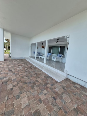 A covered outdoor area with a tiled floor, white walls, and a seating arrangement with white and blue patterned chairs.