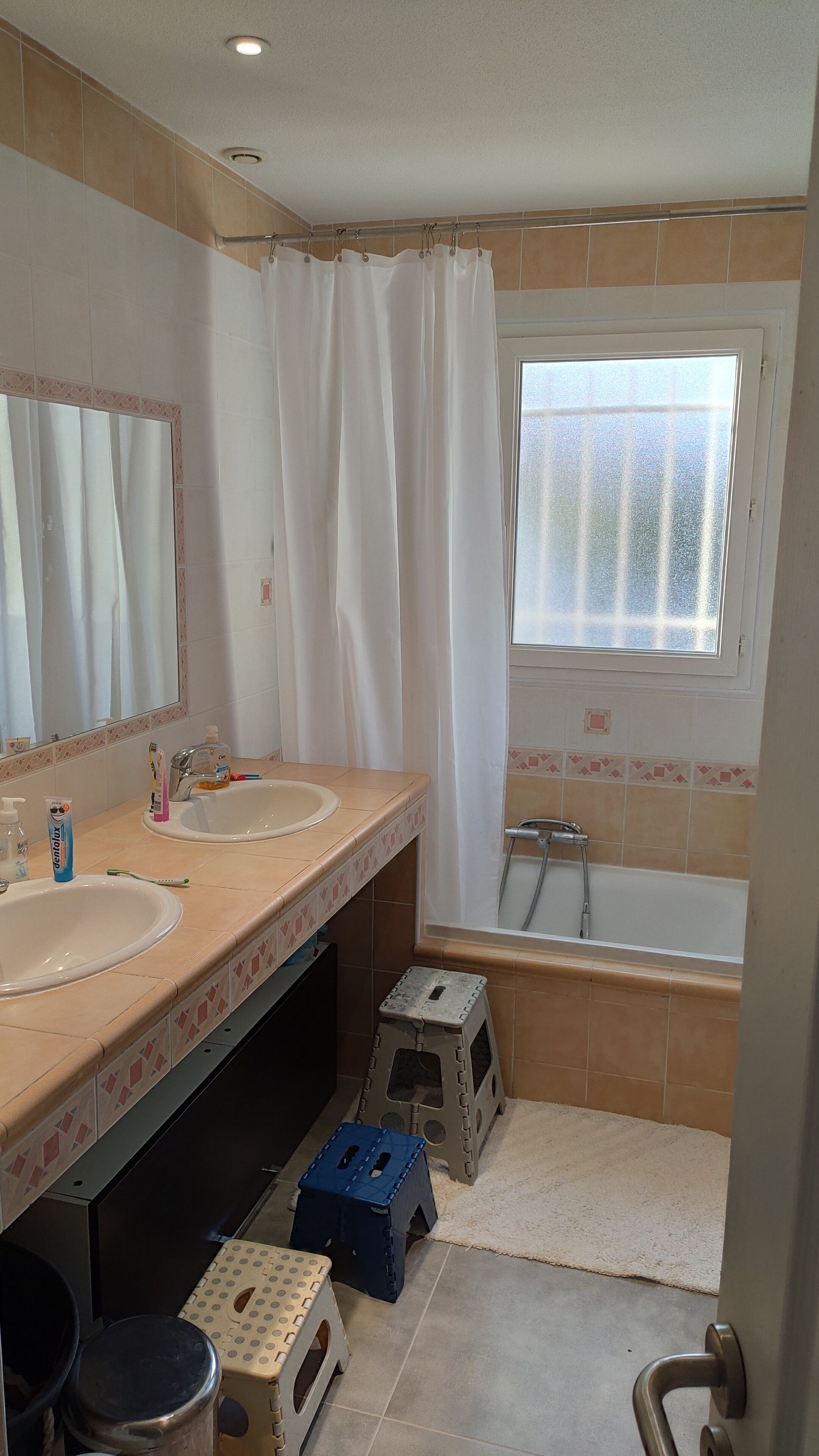 A bathroom with two sinks, a bathtub, a window, and a mirror.