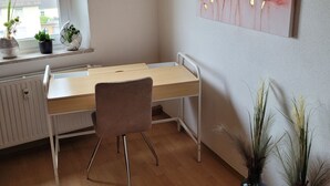 Huone, jossa on työpöytä, tuoli, patteri, ikkuna ja taideteos.