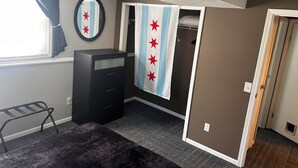 Ein Schlafzimmer mit Bett, Kommode, Spiegel, Fenster mit Vorhängen und Tür.