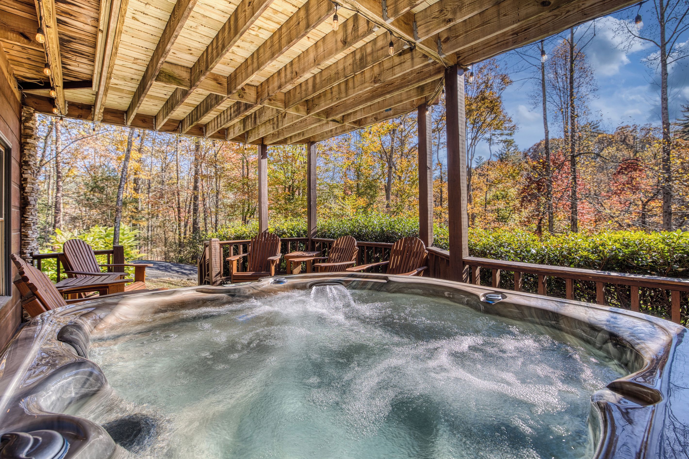 A hot tub under a wooden pergola with a view of autumn trees.