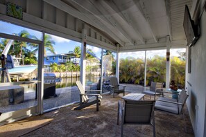 A covered outdoor area with seating and a grill, overlooking a pool and palm trees.