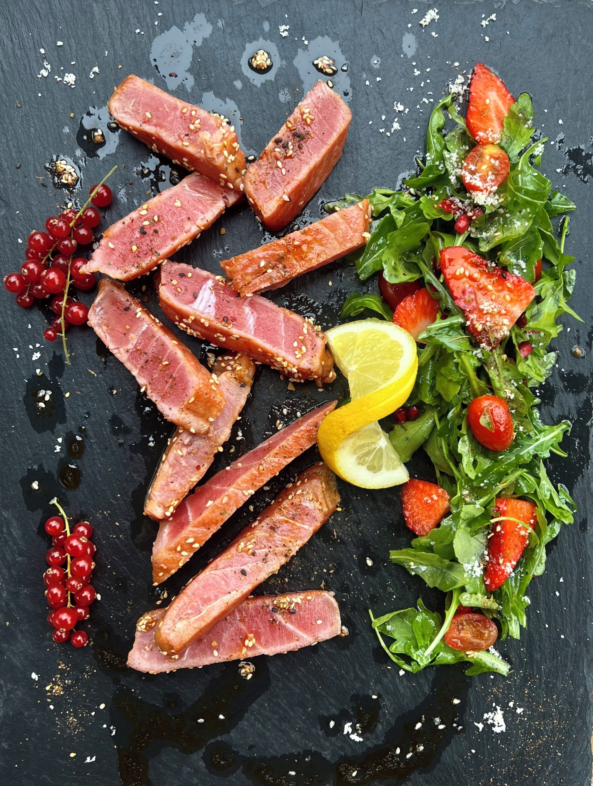 A black slate serving platter with sliced meat, cherry tomatoes, and a lemon wedge.
