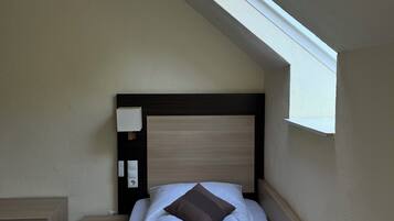 A hotel room with a bed, a nightstand, a lamp, and a skylight.