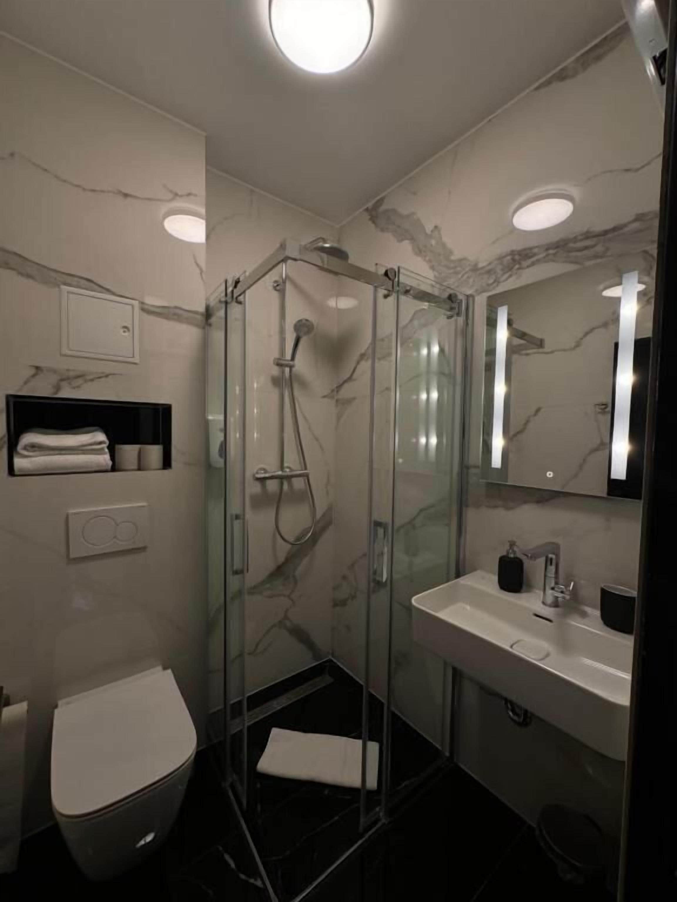 Een moderne badkamer met een douchecabine van glas, een wit toilet en een wastafel betegeld met marmer.