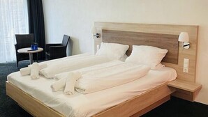 Una habitación de hotel con una cama grande, una mesita, una silla y una lámpara.