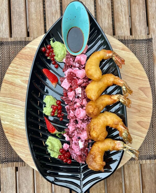 Un plato negro con camarones, fresas y salsa verde sobre una mesa de madera.