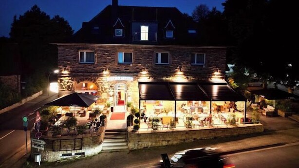 Un edificio de piedra con un patio de restaurante, mesas al aire libre y una escalera de piedra que lleva a la entrada.