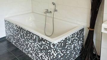 A modern bathroom with a freestanding bathtub, tiled walls, and a broom beside it.