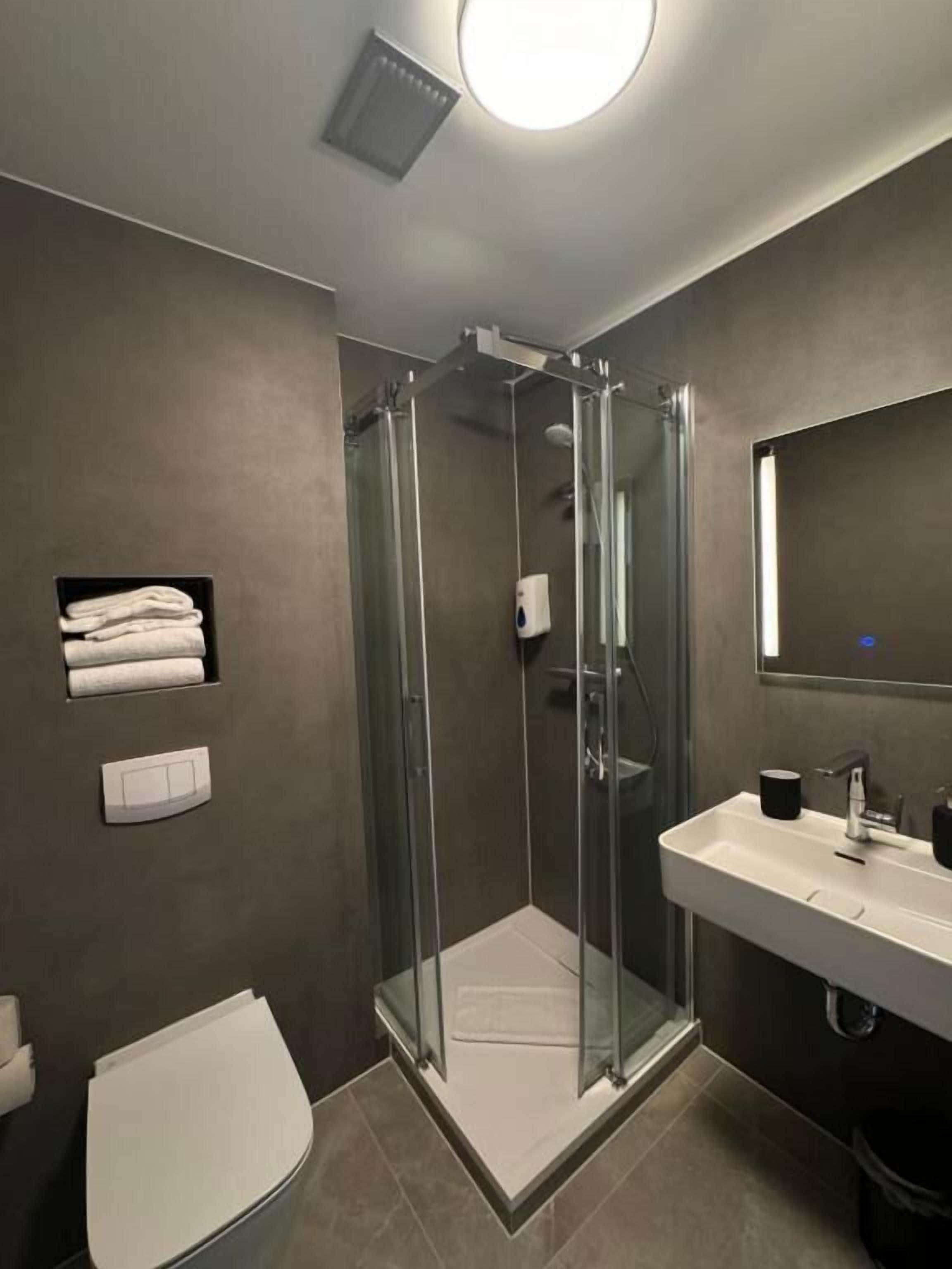 A modern bathroom with a glass-enclosed shower, a white sink, and a toilet.