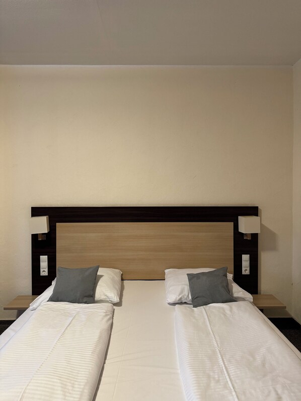 A double bed with a wooden headboard, two bedside tables with lamps, and a neutral-colored wall.