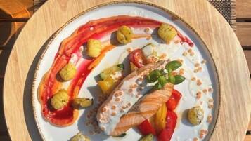 Een bord met zalm, groenten en saus op een houten tafel.
