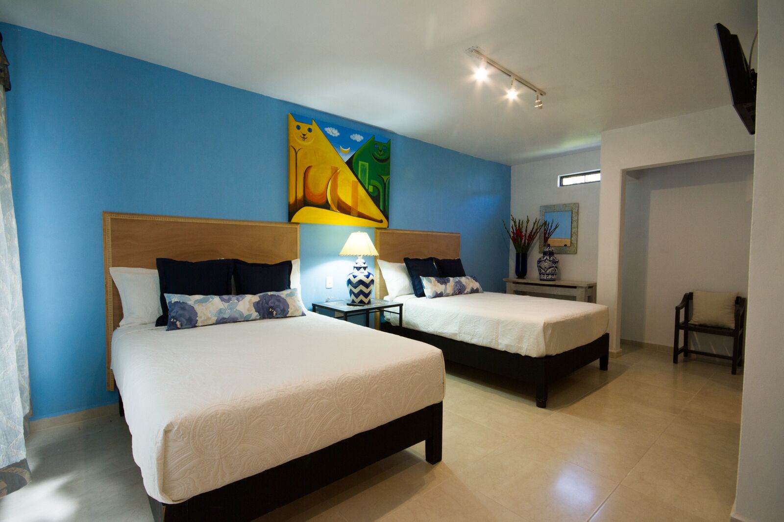 A hotel room with two beds, a nightstand with a lamp, a painting on the wall, and a chair in the corner.
