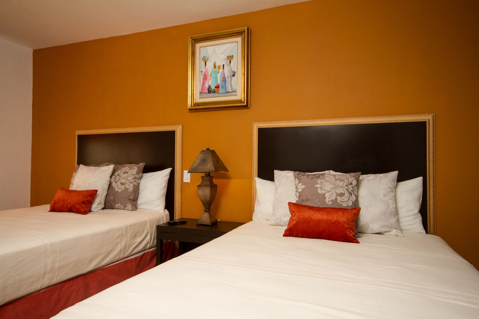 Habitación de hotel con dos camas, cada una con cabecera, mesita de noche con lámpara y un cuadro en la pared.