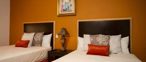 Habitación de hotel con dos camas, cada una con cabecera, mesita de noche con lámpara y un cuadro en la pared.