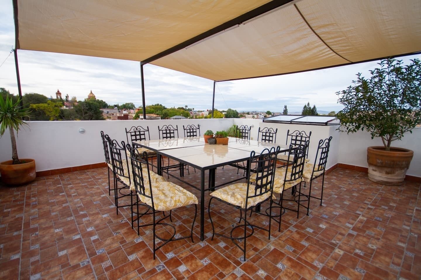 A covered patio with a table and chairs, potted plants, and a view of the cityscape.