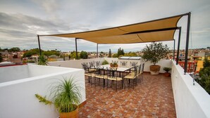 Une terrasse sur le toit, avec une table et des chaises, entourée de plantes en pot et d’un grand auvent.