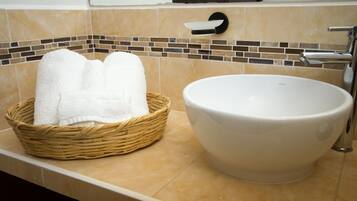A bathroom with a large white ceramic sink, a wicker basket with white towels, and a tiled backsplash.