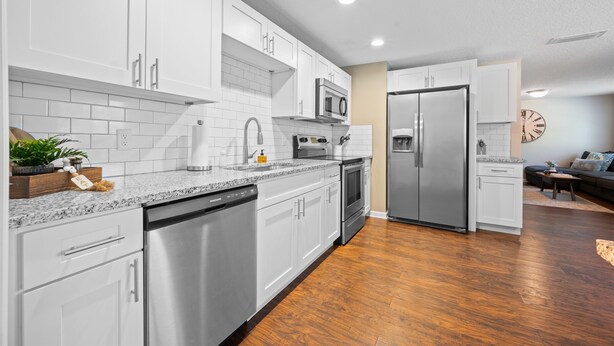 A modern kitchen with white cabinets, stainless steel appliances, and a wooden floor. - Hidden 💎 GEM with Pool Table (Jacksonville)