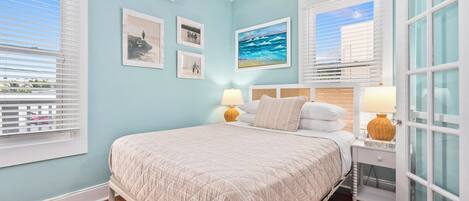 A bedroom with a bed, two bedside lamps, a window with blinds, and wall-mounted air conditioning.