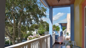 A covered porch with a railing, a small table with a plant, and a view of a street with trees and a building. - DELUXE STUDIO KING ROOM 11 AT OLD COLORADO INN (Stuart)
