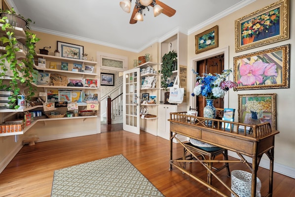 Um quarto com piso de madeira, uma escada, uma sala de jantar com mesa e cadeiras, e prateleiras com diversos objetos.