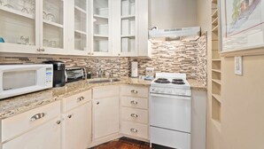 A kitchen with white cabinets, a microwave, a stove, and a tiled backsplash. - LUXURY SUITE KING AT OLD COLORADO INN (Stuart)