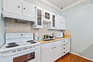 A kitchen with white cabinets, a stove, a microwave, and a sink.